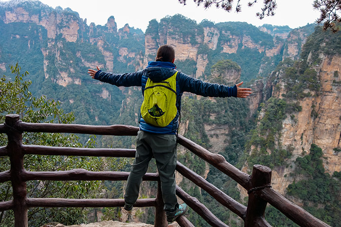 Nic standing on a fence with their arms out stretched looking out over the vista of the mountains and pillars when visiting zhangjiajie, china