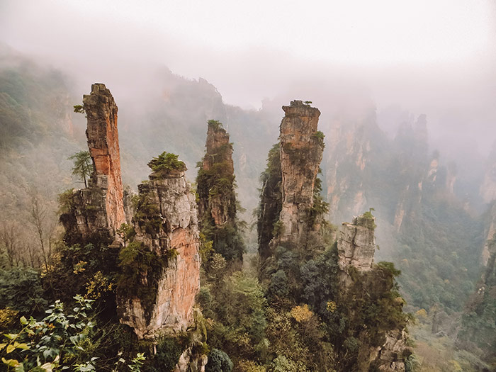 avatar like sandstone pillars sticking out over a foggy valley with mountain in the distance when visiting zhangjiajie, china