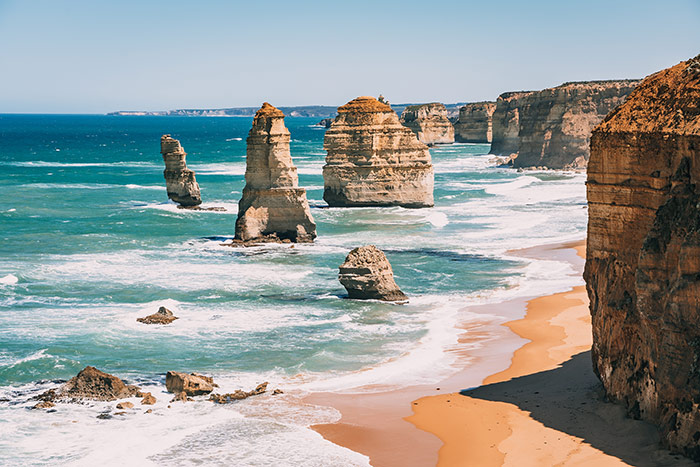The 12 apostle rock formations/ sea stacks off the coast of Great Ocean Road near Melbourne, Victoria, Australia. The blue water is breaking at the bottom of them and the golden beach sits below a tall cliff.