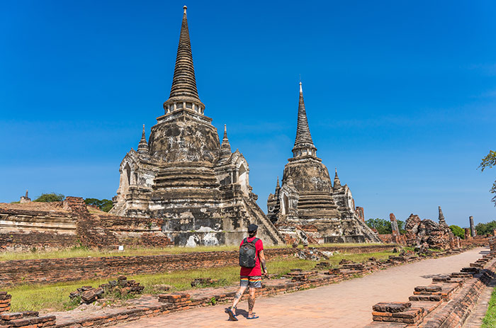 Nic walking on a blue bird day next to two massive stupas from some ancient temples in the town of Ayuthaya in Thailand