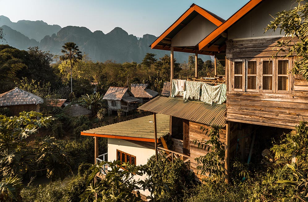 Wooden houses with washing hanging up surrounded by jungle with mountains in the distance in Vang Vieng, Laos