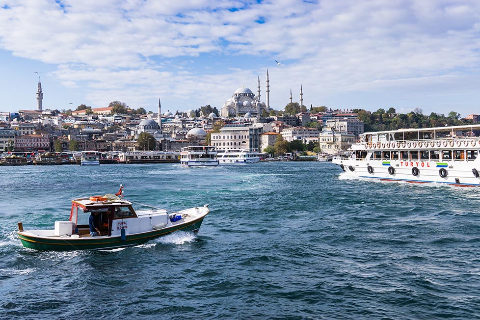 A ferry and boat crossing the water in Istanbul, Turkey with a number of large mosques in the distance
