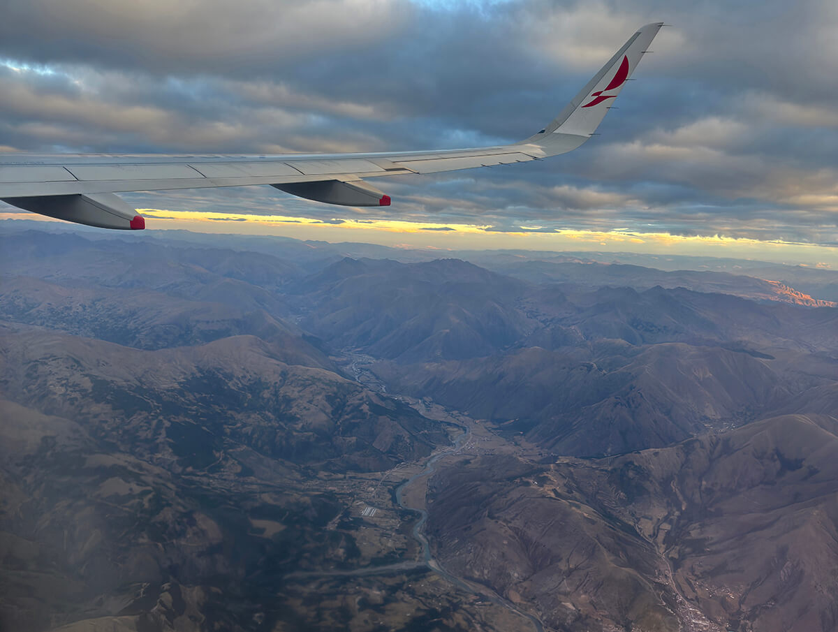 A plane flying over Cusco at sunset in Peru, South America with mountains and the city below.